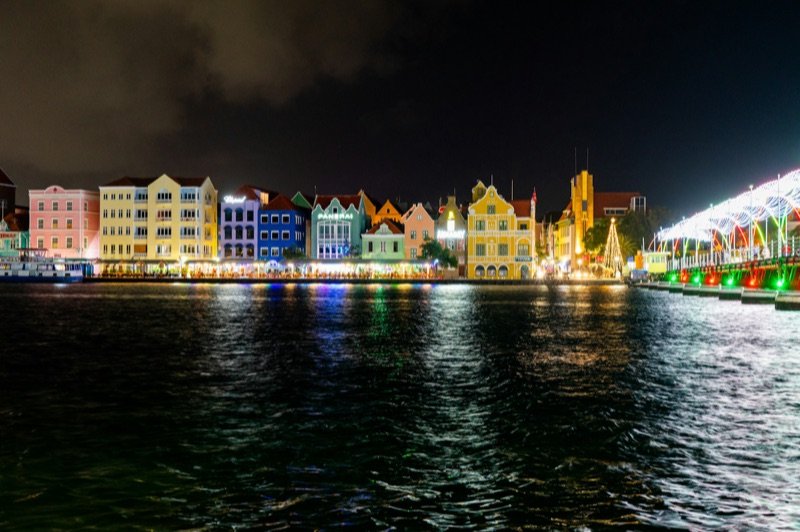 Willemstad's Handelskade waterfront lit up at night, reflected in the harbour